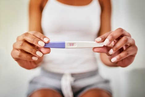 Woman sitting down, holding a positive pregnancy test wondering how to tell people