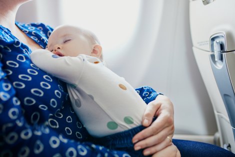 Mother holds her sleeping baby on a plane