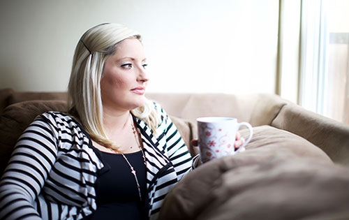 Pregnant woman drinking tea in her living room, thinking "I'm giving my baby up for adoption at birth"