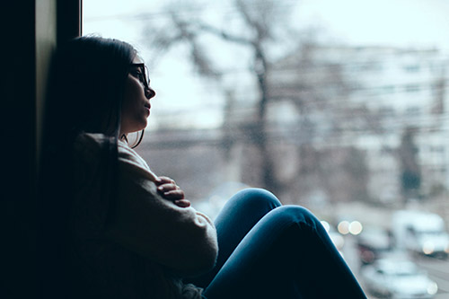 Sad young woman sits on her window sill on a cloudy day