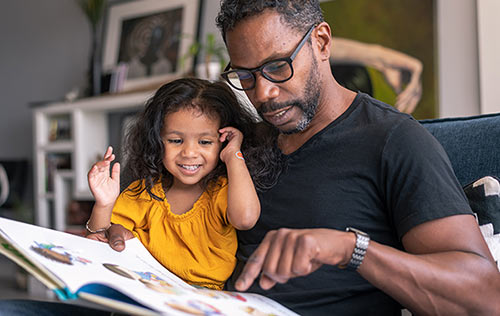 Adoptive father reads to his daughter from their vast library of children's books on adoption