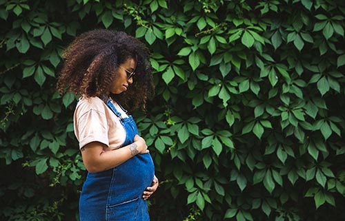 Black pregnant woman outside looks down at her baby belly