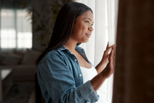pregnant woman looking out the window at home, wondering the common reasons why women choose adoption