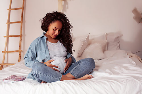 Young pretty African American expectant mother in bed, wondering 'Will the adoptive couple love my baby?'